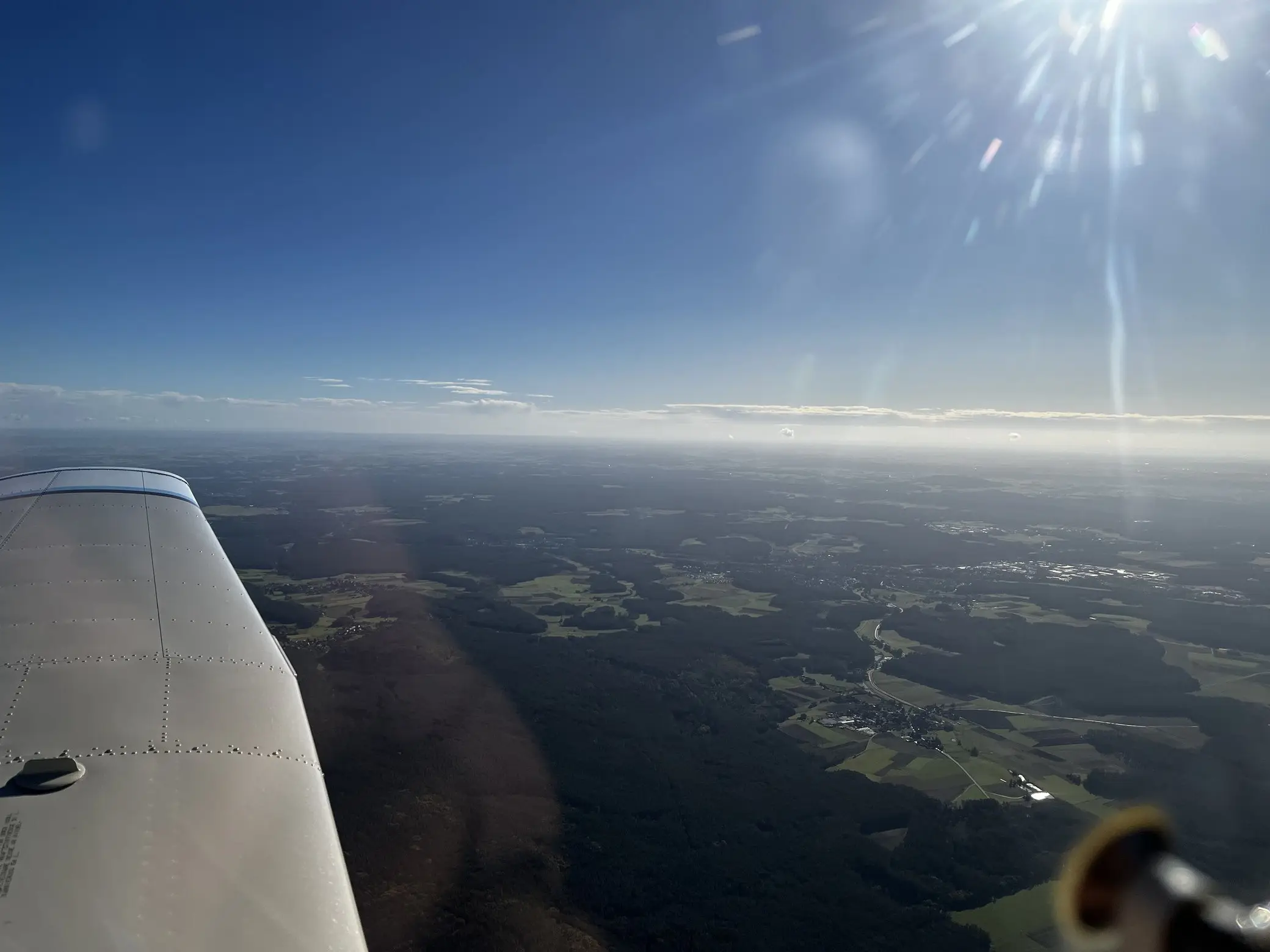 Tragfläche vor weiter, dunstiger Landschaft; die Sonne steht tief und lässt den Horizont verschwimmen