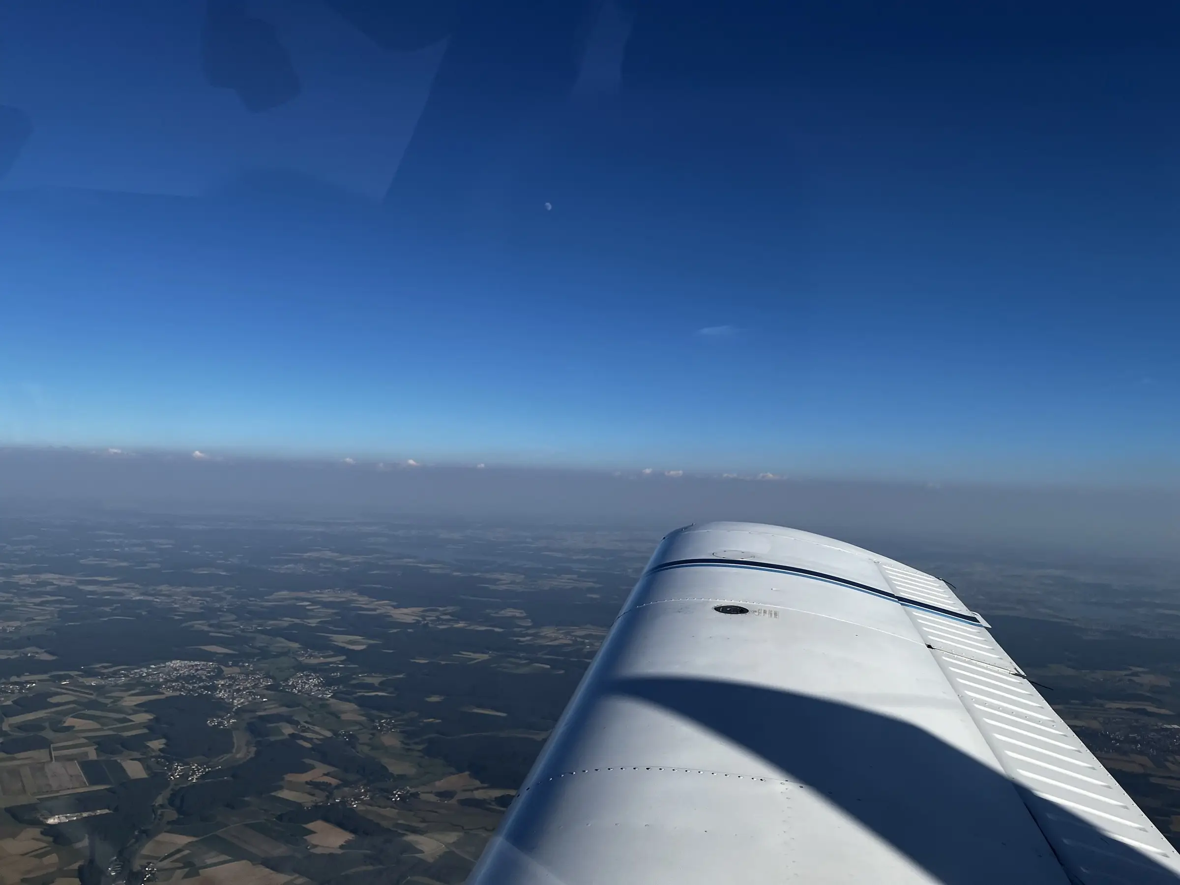 Blick über die rechte Tragfläche auf die Landschaft, darüber ein tiefblauer, klarer Sommerhimmel